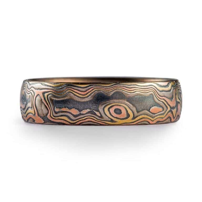 Mokume Gane band is shown in the Woodgrain pattern and the Firestorm metal combination, with a low dome profile, and an etched and oxidized finish. Firestorm features 14k red gold, 14k yellow gold, Palladium, and sterling silver.