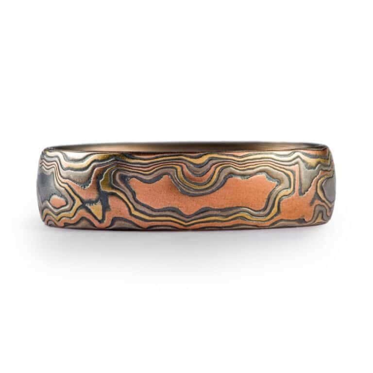 Mokume Gane band is shown in the Woodgrain pattern and the Firestorm metal combination, with a low dome profile, and an etched and oxidized finish. Firestorm features 14k red gold, 14k yellow gold, Palladium, and sterling silver.