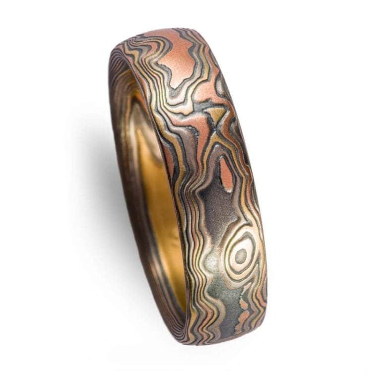 Mokume Gane band is shown in the Woodgrain pattern and the Firestorm metal combination, with a low dome profile, and an etched and oxidized finish. Firestorm features 14k red gold, 14k yellow gold, Palladium, and sterling silver.