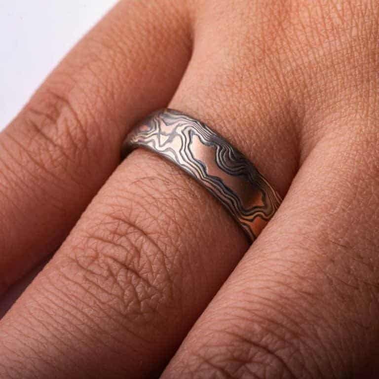 Mokume Gane band is shown in the Woodgrain pattern and the Firestorm metal combination, with a low dome profile, and an etched and oxidized finish. Firestorm features 14k red gold, 14k yellow gold, Palladium, and sterling silver.