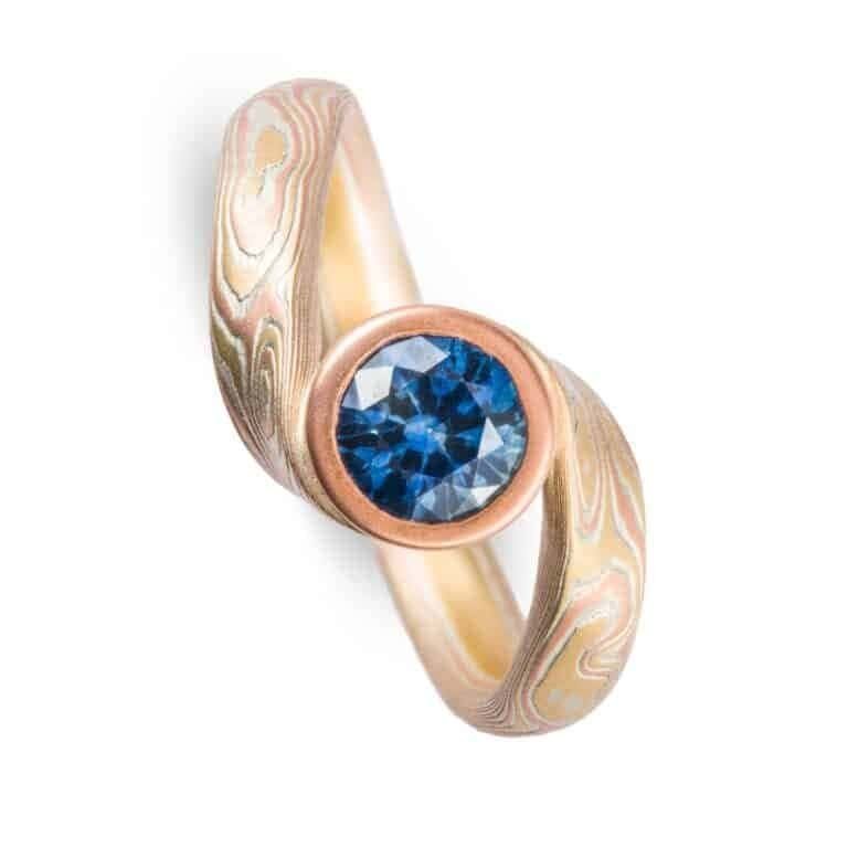 deep blue sapphire circled with red gold and yellow gold and silver in woodgrain patterned ring