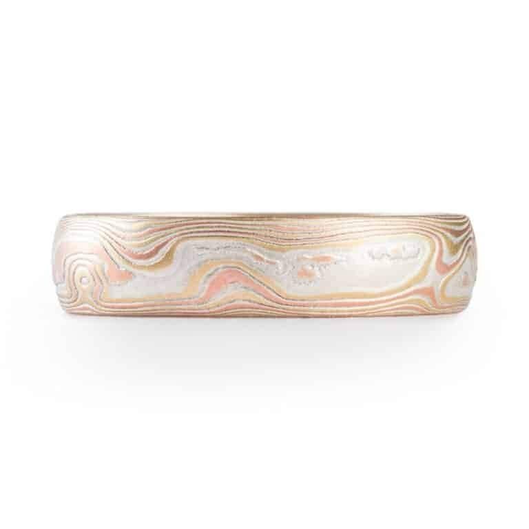 simple and lovely mokume gane wedding ring in fire palette with red and yellow golds and blue sapphire flush set in