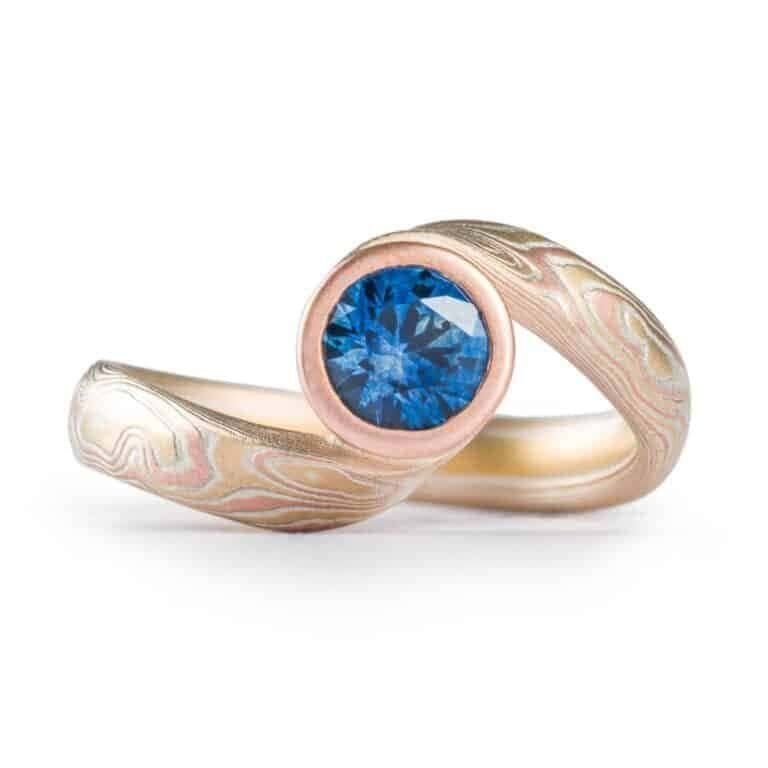 deep blue sapphire circled with red gold and yellow gold and silver in woodgrain patterned ring