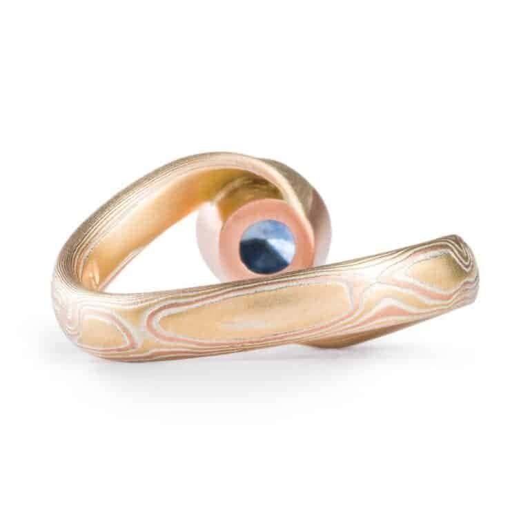 deep blue sapphire circled with red gold and yellow gold and silver in woodgrain patterned ring