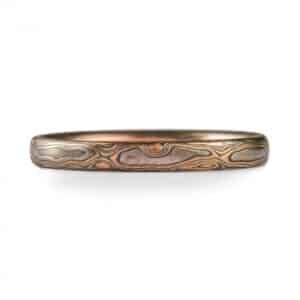 A low dome Mokume Gane band in Woodgrain pattern and Firestorm metal combo with etched and oxidized finish, made of 14k red gold, 14k yellow gold, palladium, and sterling silver.