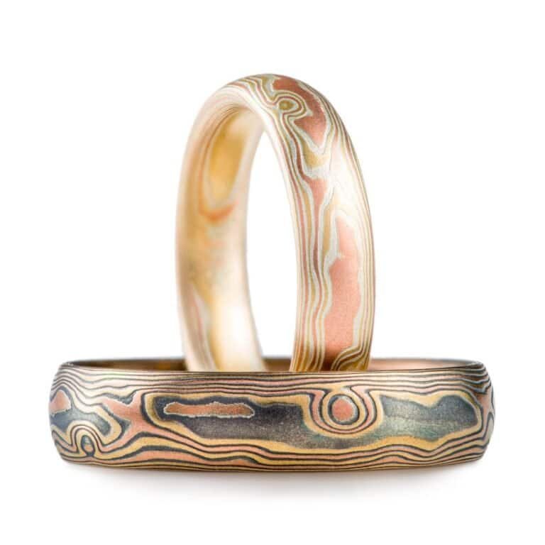 set of light and dark mokume gane woodgrain patterned rings, one narrower and lighter looking, and one wider and darker