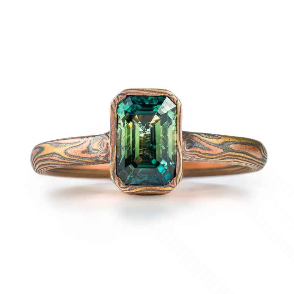 Mokume gane engagement style ring, made to look like it's made of warm toned wood grained branches, holding a rectangular emerald cut green sapphire.