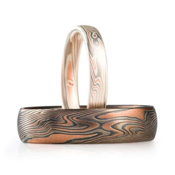 set of light and dark matching mokume gane rings, a narrower one that has a pinkish appearance, and a wider ring with a dark gray/red look