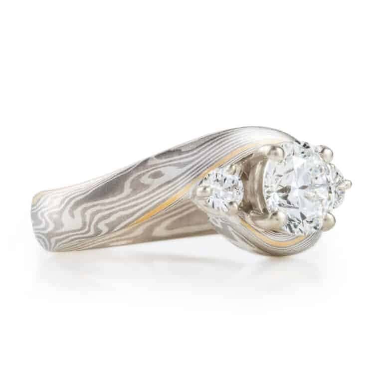 mokume gane wedding ring, band is twisted around the setting in the center, three diamonds, a larger one in the center with two smaller side stones.