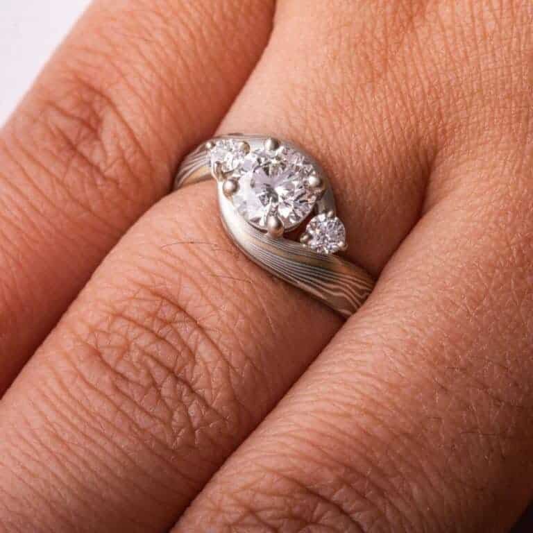 mokume gane wedding ring, band is twisted around the setting in the center, three diamonds, a larger one in the center with two smaller side stones.