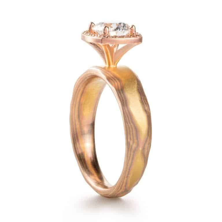 halo diamond ring with a large round stone with many small round stones around the edge with w red gold setting and yellow gold and red gold and silver mokume metal . contemporary looking