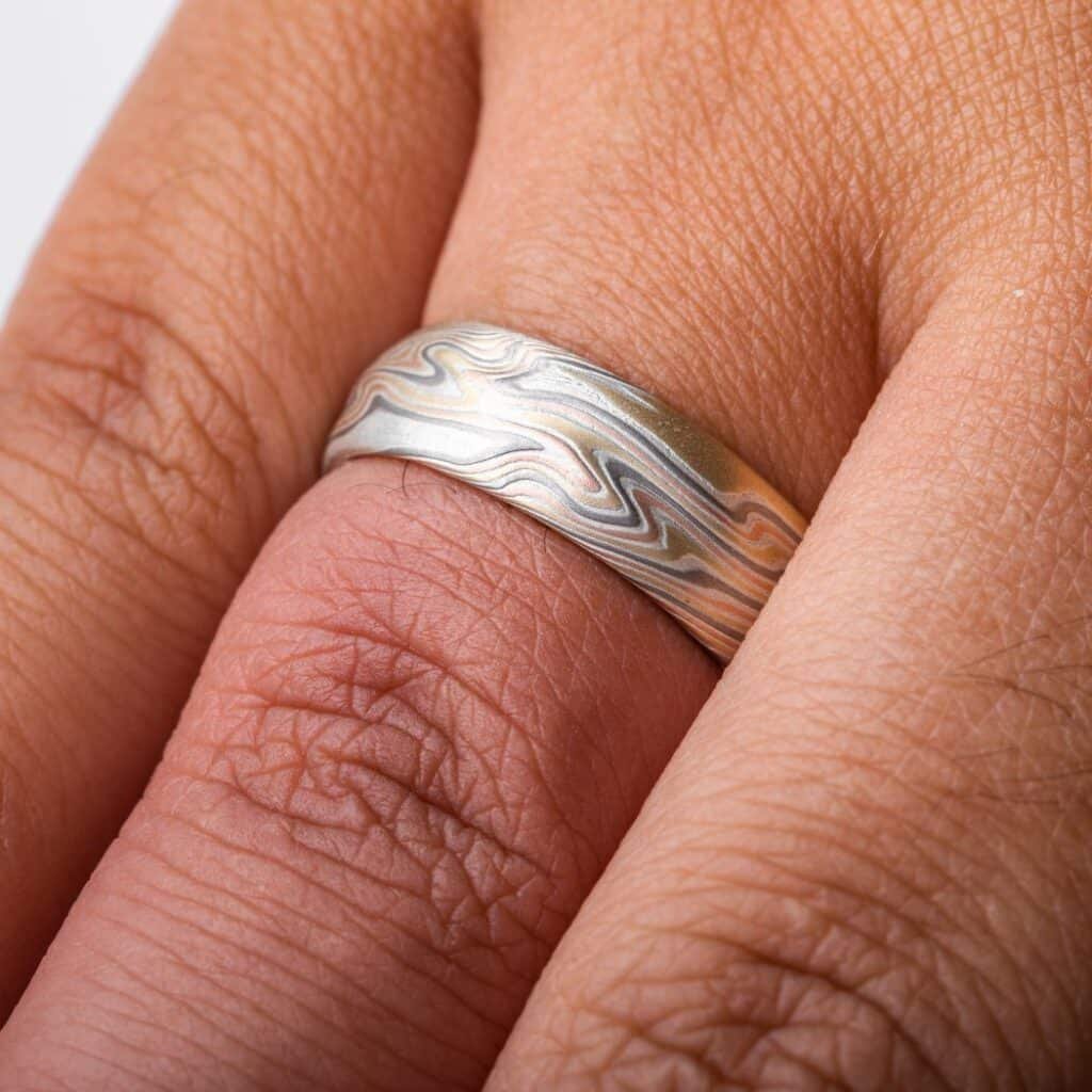 textured twist pattern ring, with a carved surface like rolling waves on the surface of water, overall light looking, made with layers of red and yellow gold, palladium and silver