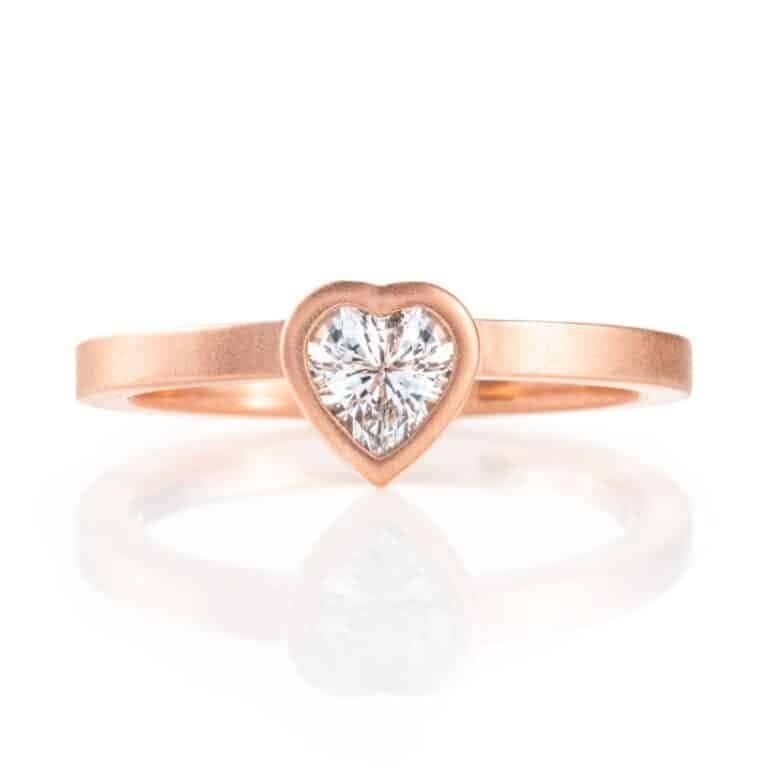 heart shaped white stone held in a bezel, a strip of metal wrapping all around the perimeter of the stone, on a band