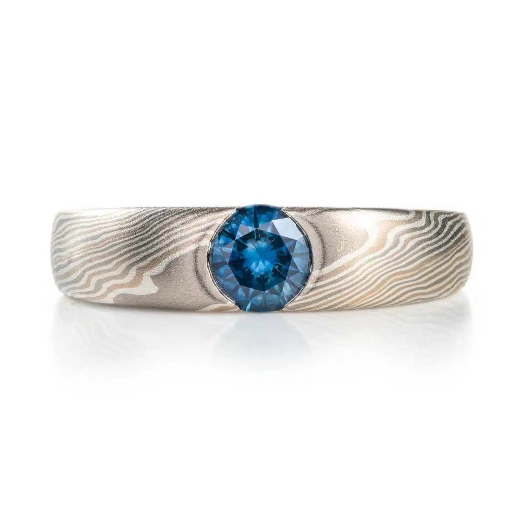 Twist patterned mokume gane ring with a flush round blue sapphire.