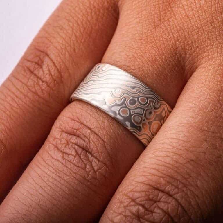 Wide ring with a flat profile, made with red gold, palladium (gray) and silver (light gray), in a twisting and speckled style pattern.  