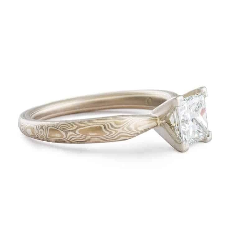 solitaire style mokume gane engagement ring with square diamond set in prongs, ring has an overall silvery palette and a woodgrain style pattern