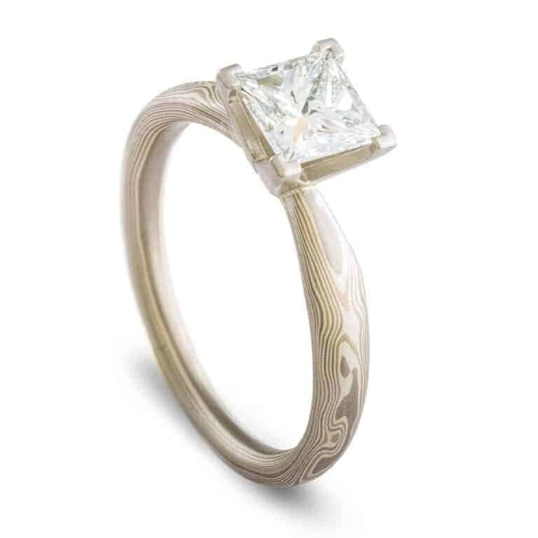 solitaire style mokume gane engagement ring with square diamond set in prongs, ring has an overall silvery palette and a woodgrain style pattern