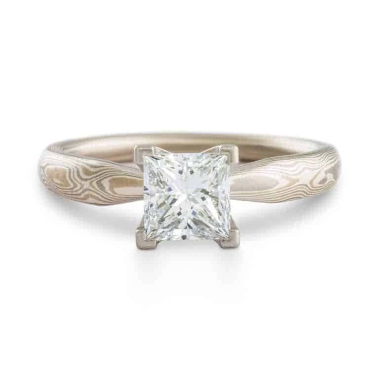 solitaire style mokume gane engagement ring with square diamond set in prongs, ring has an overall silvery palette and a woodgrain style pattern