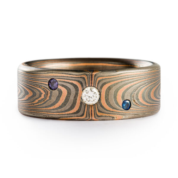 Mokume Gane 8mm wide ring made by arn krebs, vortex pattern and embers palette, flat profile, with flush set stones. The embers palette is made of red gold palladium and silver and the ring has been etched and oxidized.