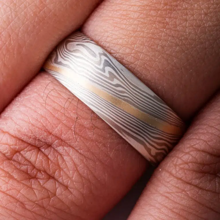 light colored mokume gane twist pattern band with a single stripe of yellow gold running around, smooth finish and domed profile