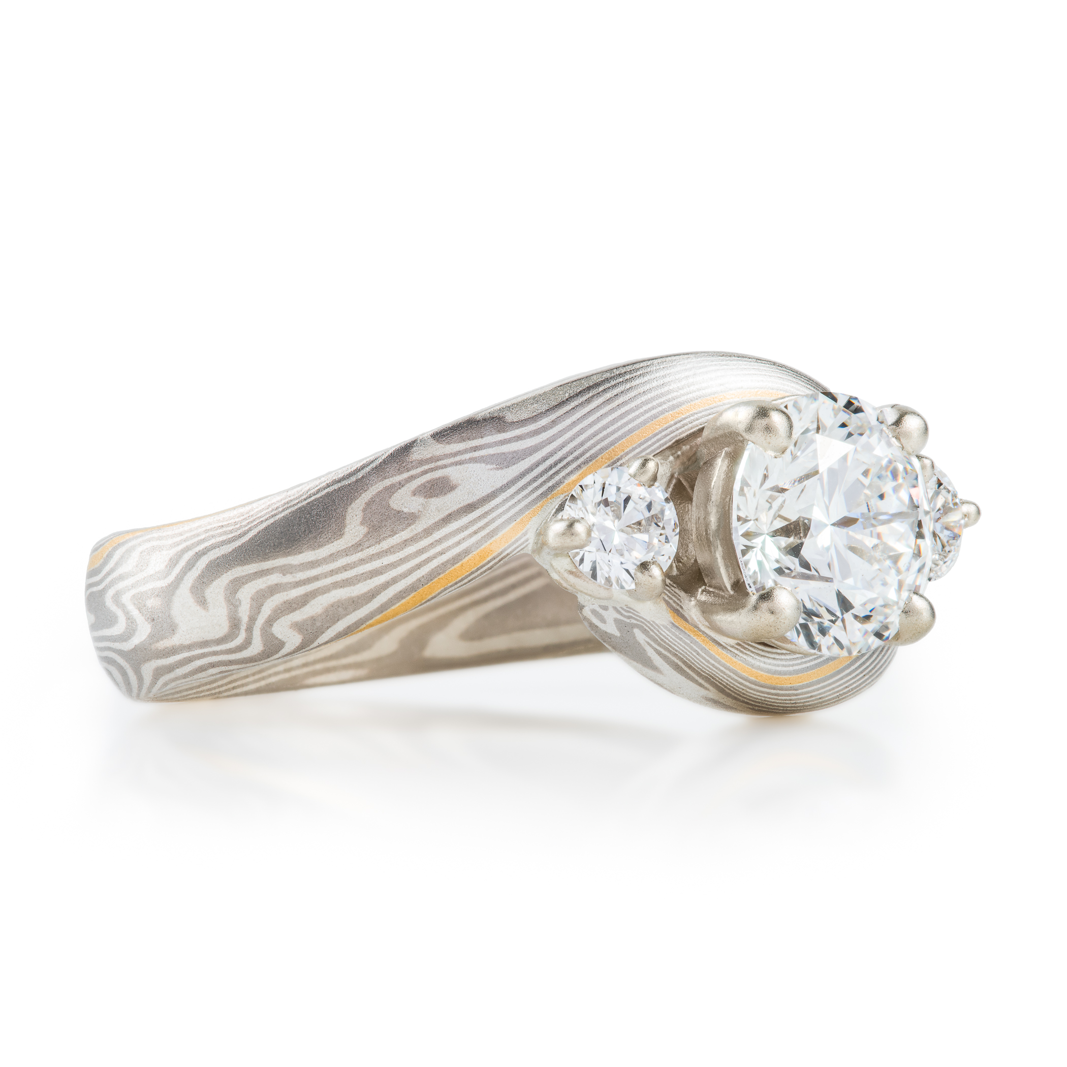 mokume gane wedding ring, band is twisted around the setting in the center, three diamonds, a larger one in the center with two smaller side stones.