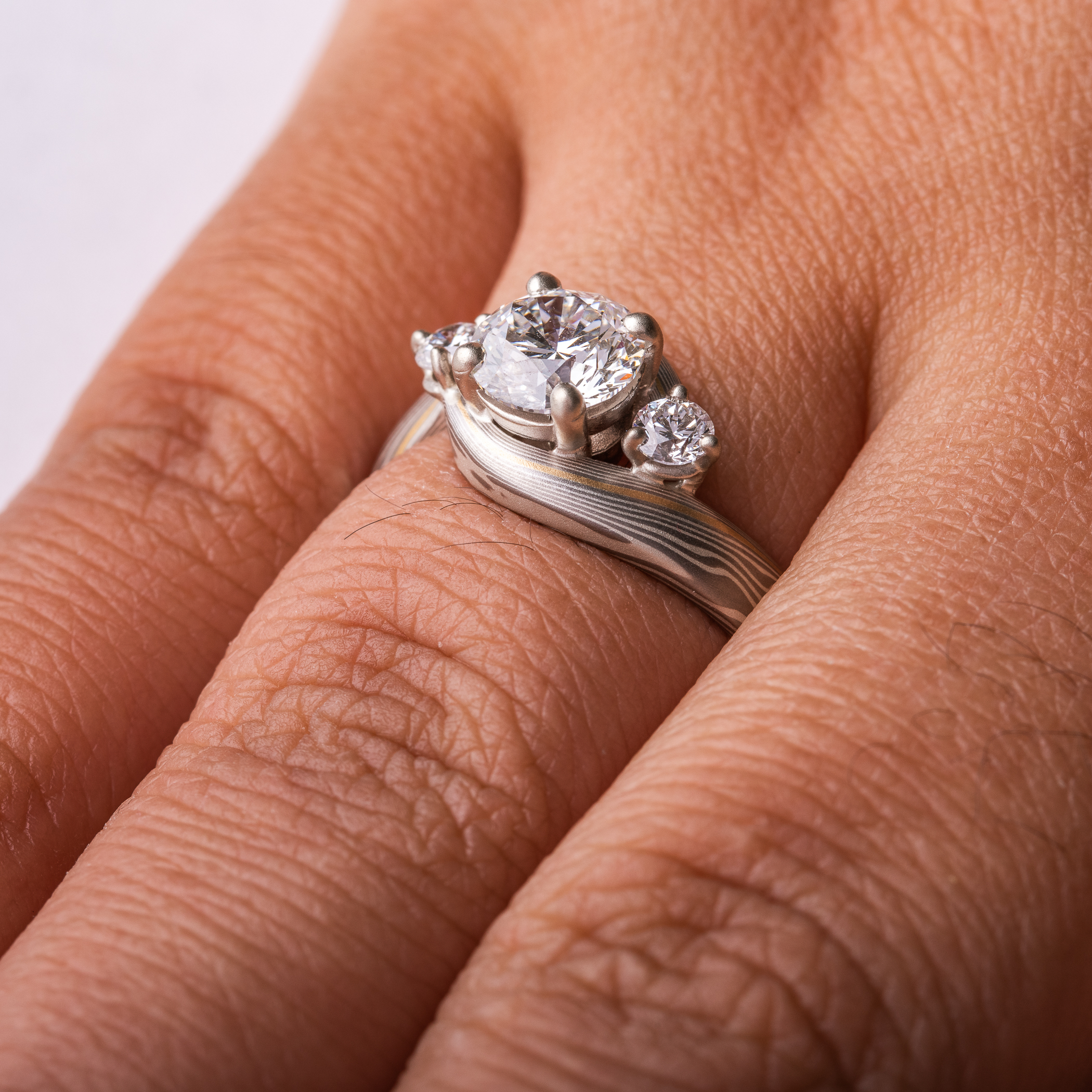 mokume gane wedding ring, band is twisted around the setting in the center, three diamonds, a larger one in the center with two smaller side stones.