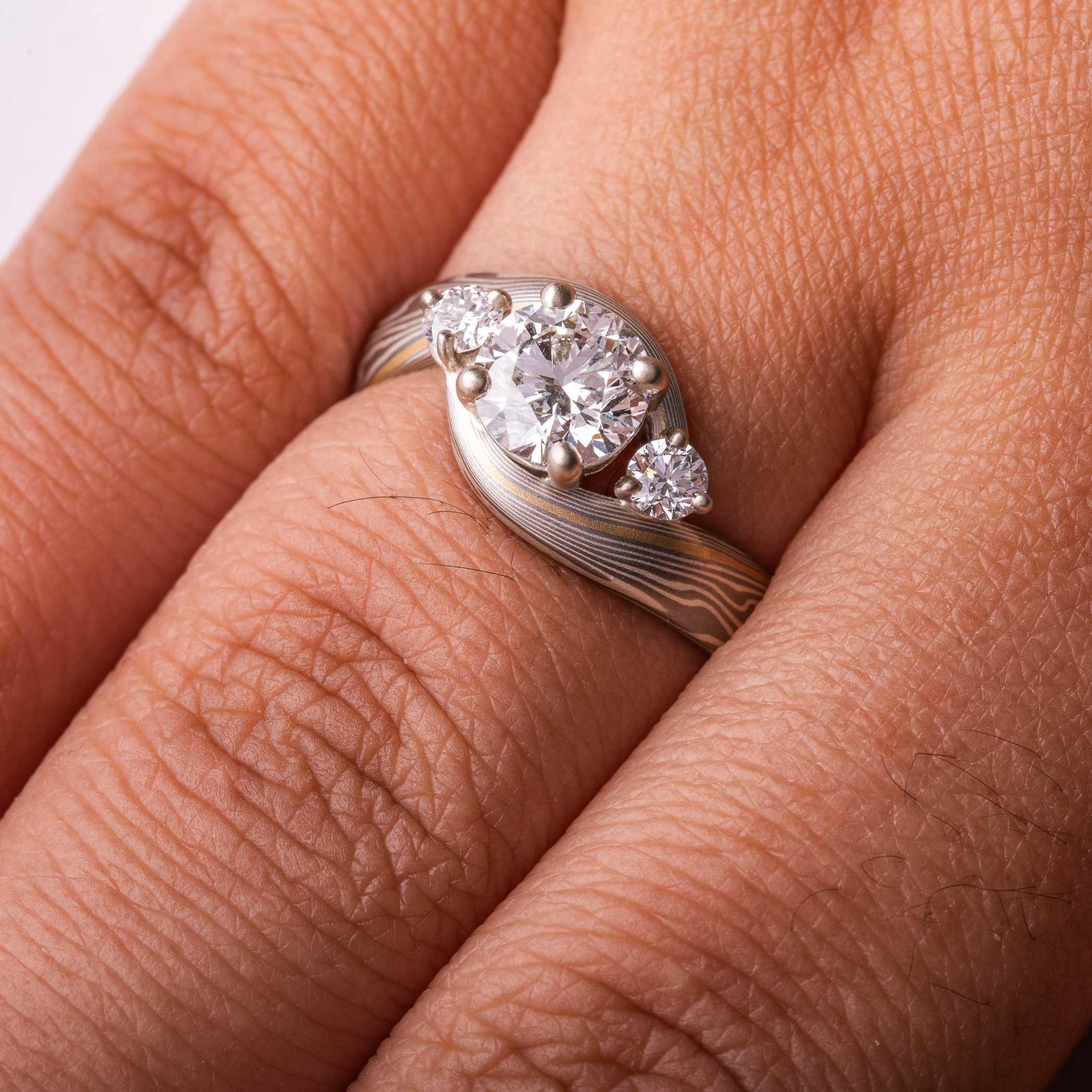 mokume gane wedding ring, band is twisted around the setting in the center, three diamonds, a larger one in the center with two smaller side stones.