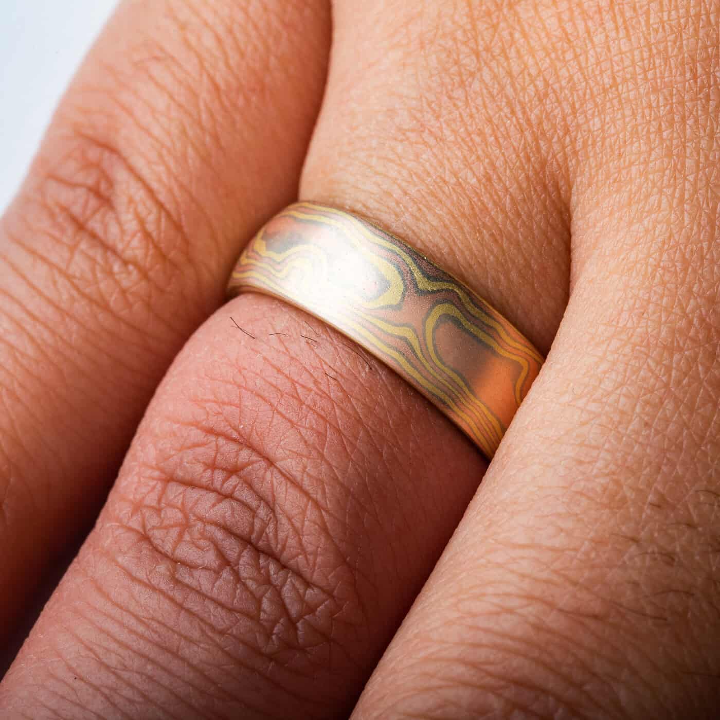 All gold mokume gane ring made in woodgrain pattern, with layers of red gold and yellow gold, and thin layers of white gold in between.