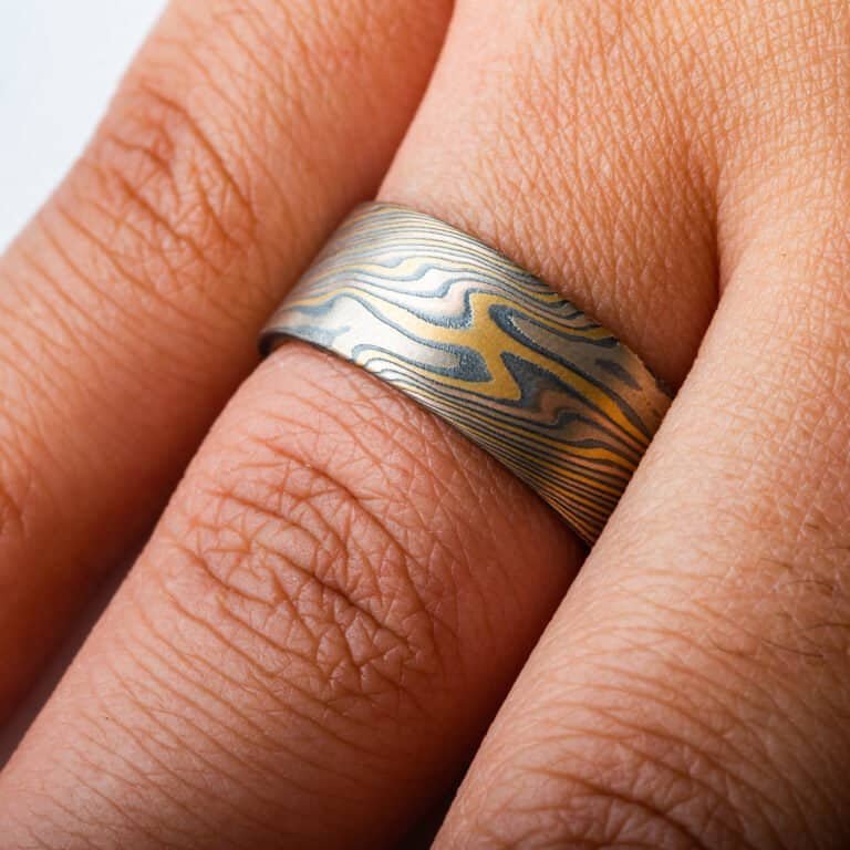 wide mokume gane twist patterned ring with a flat profile, ring is made with layers of red and yellow gold, palladium and oxidized silver