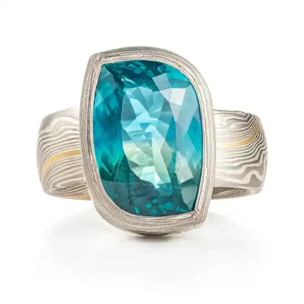 bold statement ring, mokume twist patterned band with a matching patterned bezel holding a large light green/blue slightly rectangular sapphire