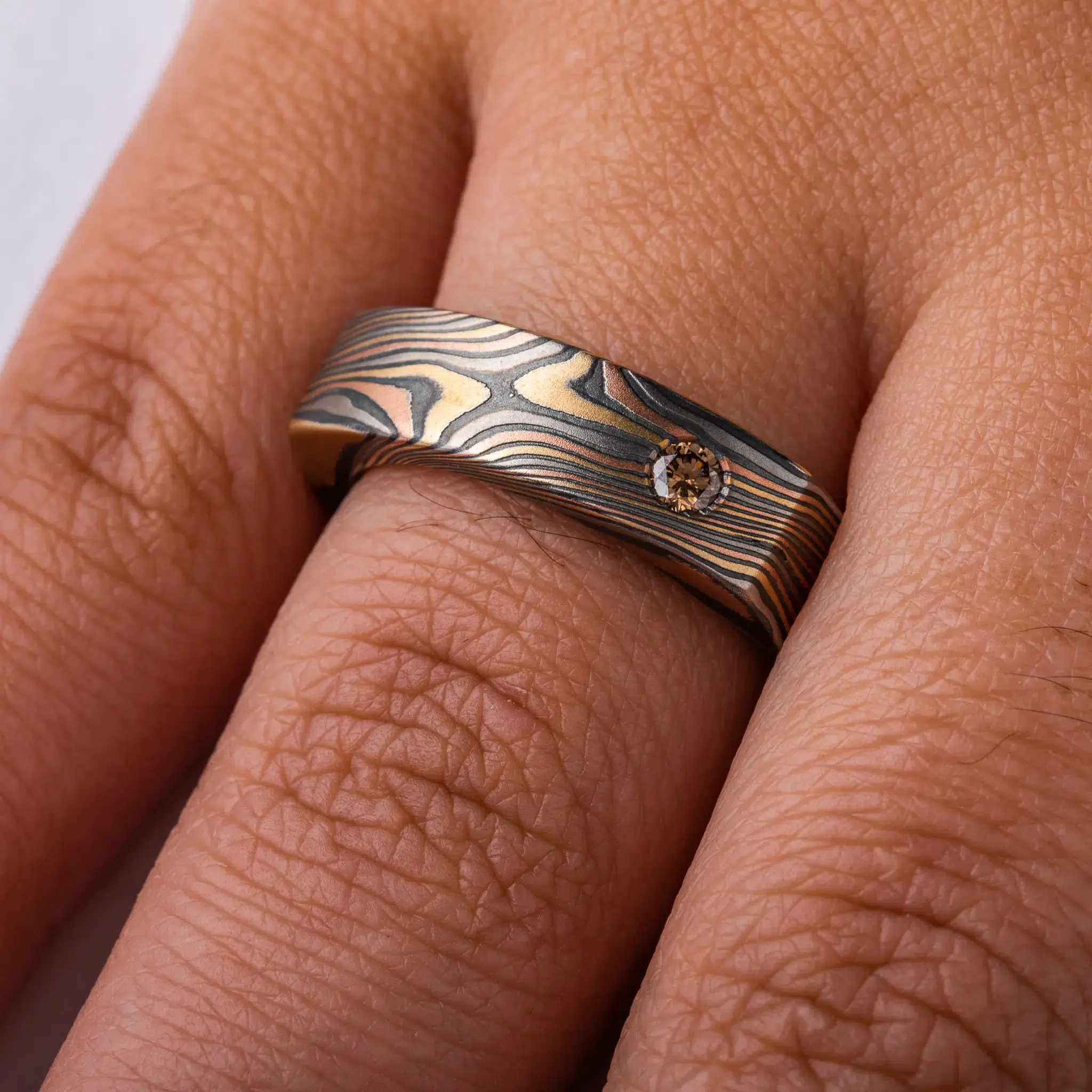 uniquely profiled soft square shaped mokume gane ring with a thicker top section - somewhat similar to a signet style ring, but rectangular, with a small cognac diamond flush set into a corner