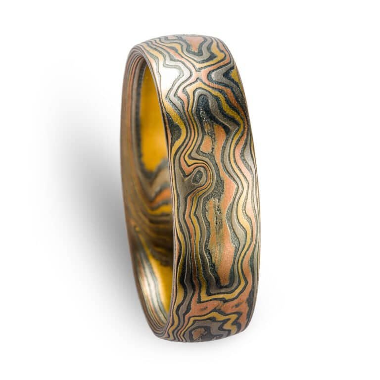 A rustic Woodgrain etched Mokume Gane band with a low dome profile and oxidized finish is made from Firestorm metal.