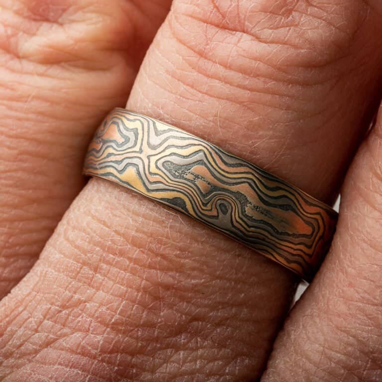 A rustic Woodgrain etched Mokume Gane band with a low dome profile and oxidized finish is made from Firestorm metal.