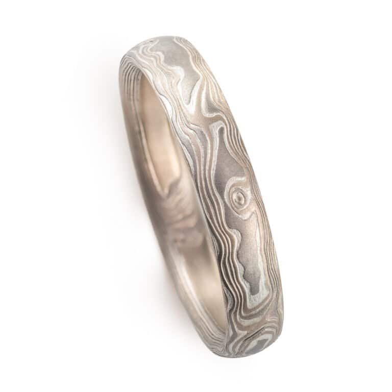 A Mokume Gane band with Woodgrain Pattern and Smoke palette, etched finish, low dome profile, featuring Palladium, 14k white gold, and sterling silver.