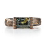 engagement style ring featuring a large rectangular australian sapphire shown in a mossy green with yellow highlights, paired with an earthy metal combination of red and yellow golds, palladium and oxidized silver