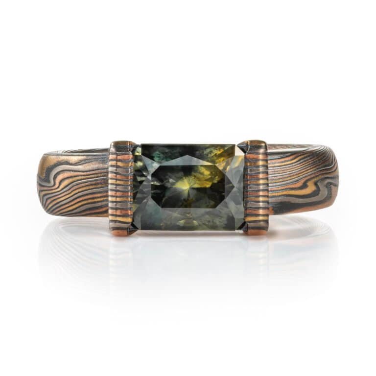 engagement style ring featuring a large rectangular australian sapphire shown in a mossy green with yellow highlights, paired with an earthy metal combination of red and yellow golds, palladium and oxidized silver