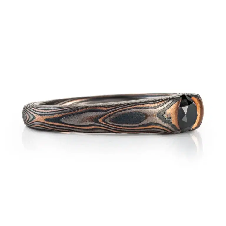 dark and moody feeling mokume gane ring, with solitaire black diamond in cathedral style setting, metals in the ring are red gold, palladium and oxidized silver