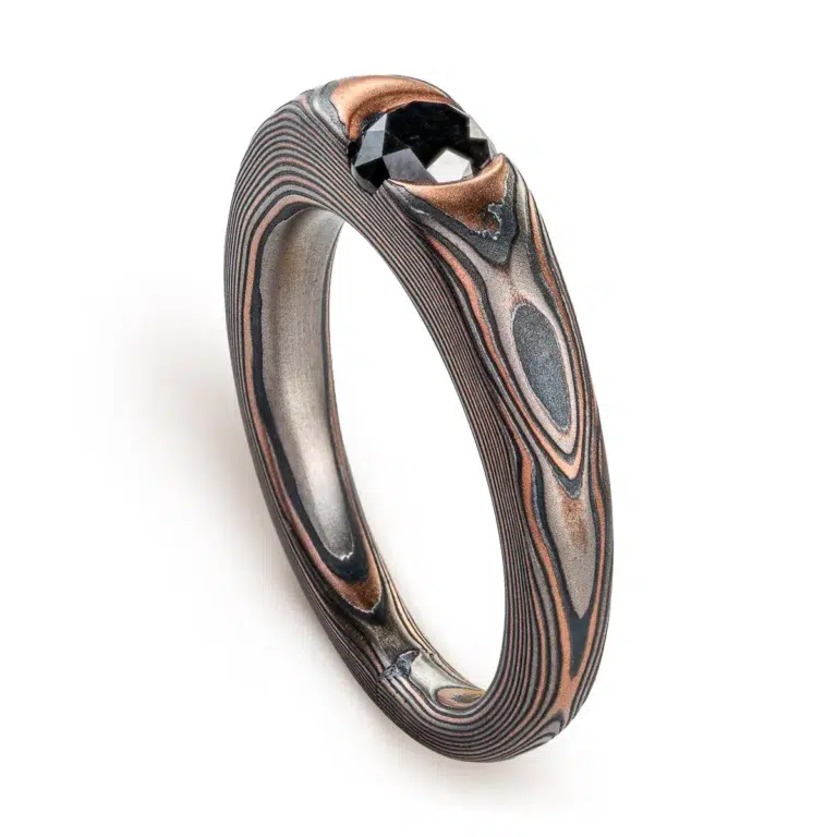 dark and moody feeling mokume gane ring, with solitaire black diamond in cathedral style setting, metals in the ring are red gold, palladium and oxidized silver