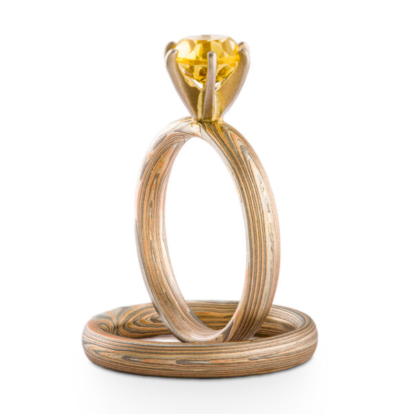 Pair of matching mokume gane bands, one ring propped upright with a yellow stone in prongs at the top.