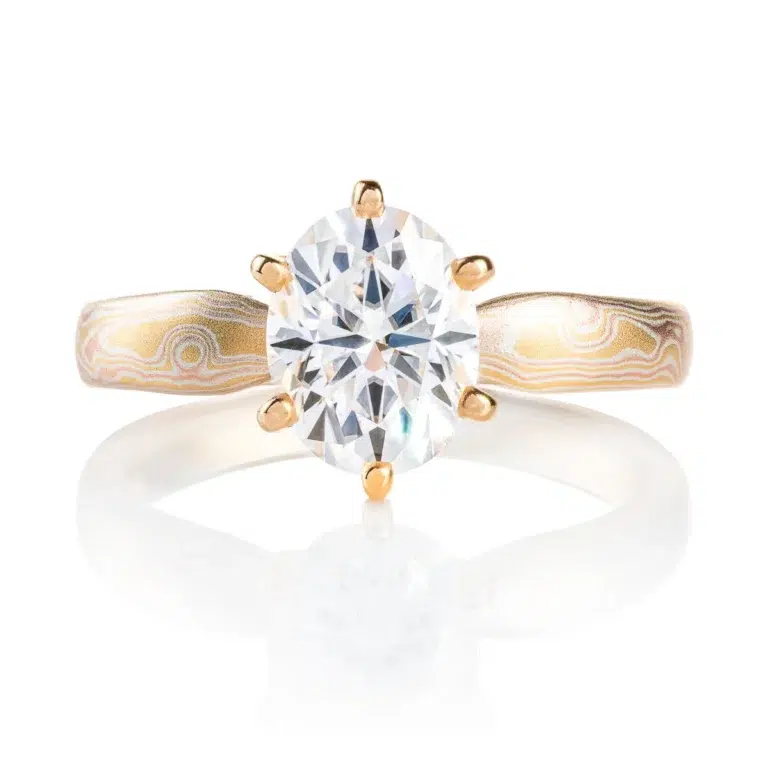 elegant six prong style engagement ring with an oval shaped diamond, band is woodgrain patterned and made in 18kt gold