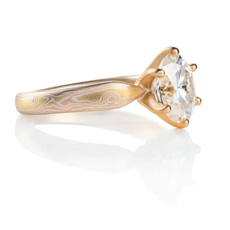 elegant six prong style engagement ring with an oval shaped diamond, band is woodgrain patterned and made in 18kt gold