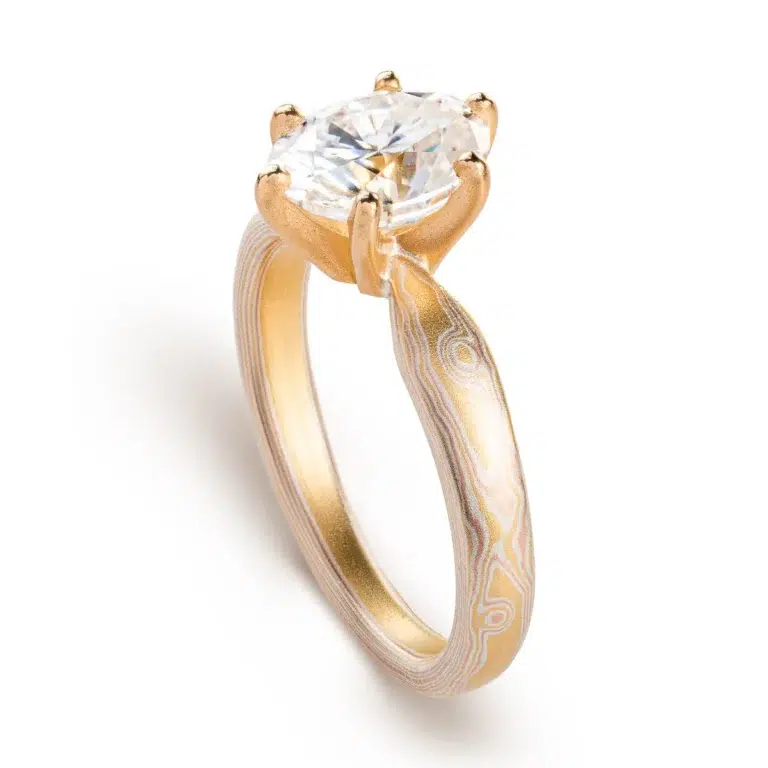 elegant six prong style engagement ring with an oval shaped diamond, band is woodgrain patterned and made in 18kt gold