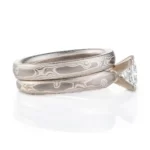 pair of stacked mokume gane bands, one plain, one with a square diamond set in prongs, both patterned in woodgrain style