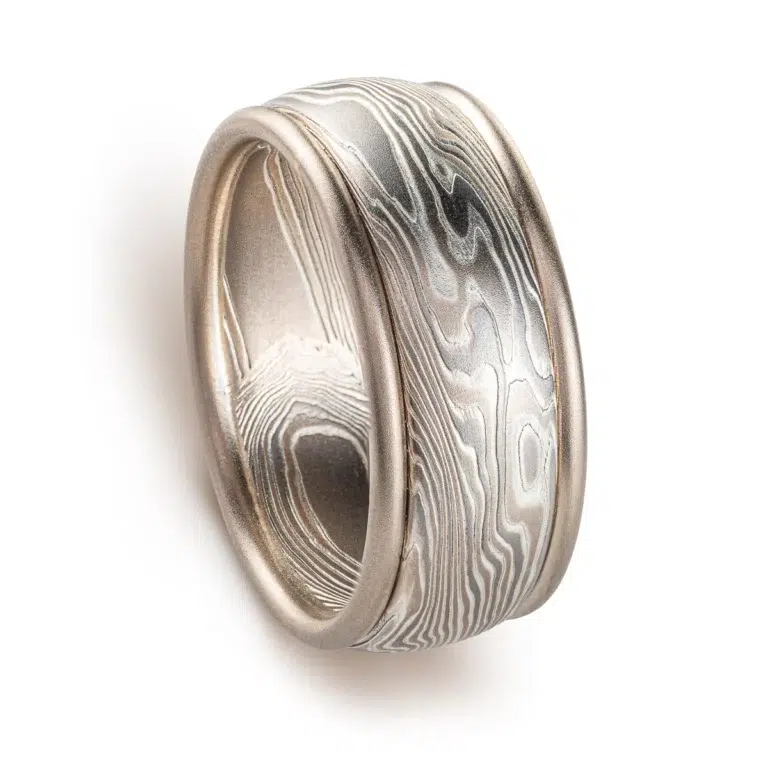 mokume gane twisted pattern ring made of layers of metal in different shades of gray, the ring also has added rails running around the top and bottom edges