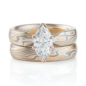 pair of stacked rings patterned in mokume twist style, the ring on top has a single marquise shaped diamond, that is wider than the band it is on and hangs over the front of the band underneath it