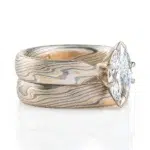 pair of stacked rings patterned in mokume twist style, the ring on top has a single marquise shaped diamond, that is wider than the band it is on and hangs over the front of the band underneath it