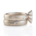 pair of stacked rings patterned in mokume twist style, the ring on top has a single marquise shaped diamond, that is wider than the band it is on and hangs over the front of the band underneath it