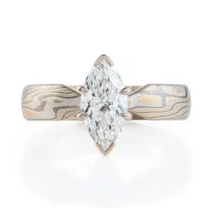 ring with a solitaire stone set in prongs, featuring marquise shaped white stone, band portion is made with yellow gold, palladium and sterling silver