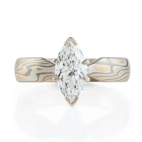 ring with a solitaire stone set in prongs, featuring marquise shaped white stone, band portion is made with yellow gold, palladium and sterling silver