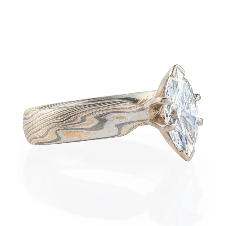 ring with a solitaire stone set in prongs, featuring marquise shaped white stone, band portion is made with yellow gold, palladium and sterling silver